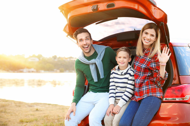 Young family with cute boy sitting in car trunk near river - 写真・画像