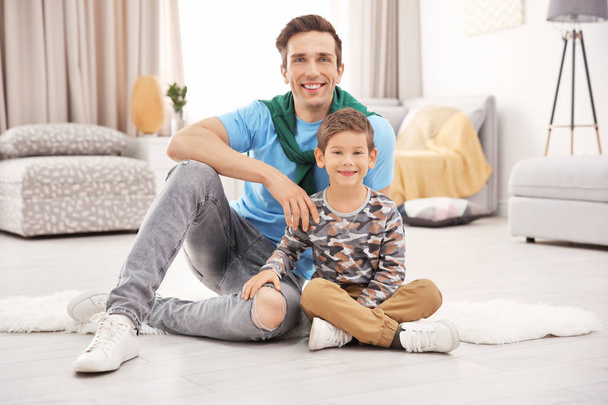 Portrait of father and son sitting on floor at home - Φωτογραφία, εικόνα