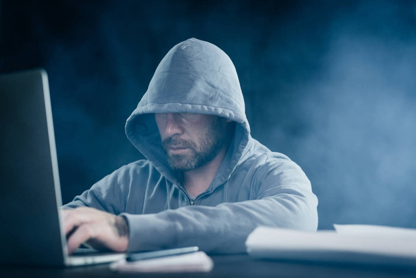 hombre barbudo misterioso esconde su cara bajo el capó, hackea la computadora portátil
 - Foto, Imagen