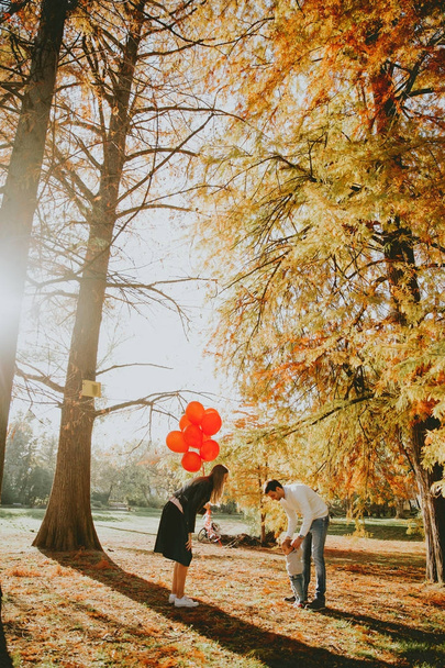 Happy young parents have fun with baby boy in autumn park holding red balloons - Foto, Bild