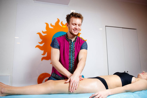 Концепція масажу та здоров'я. Чоловічий масажист робить лімфатичний дренаж і масаж для тонування м'язів дівчини в чорній білизні на столі в фізіологічній кімнаті
. - Фото, зображення