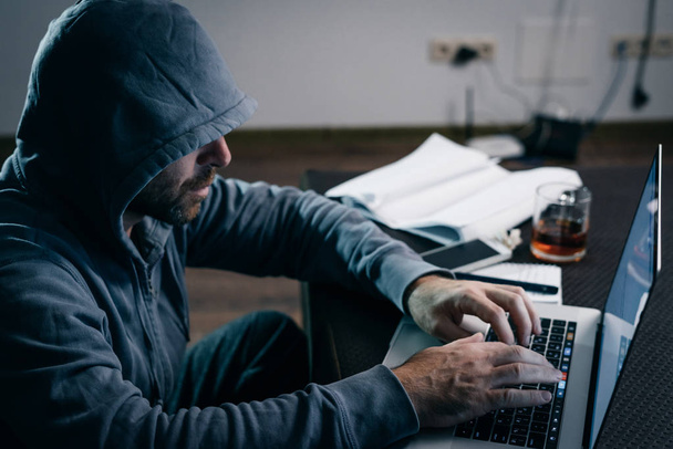 guy hacker in a sweatshirt with a hood prints on a laptop - Foto, Imagem