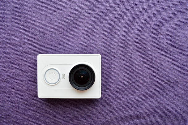 Valkoinen toimintakamera, jossa on suuri musta linssi violetilla taustalla
 - Valokuva, kuva