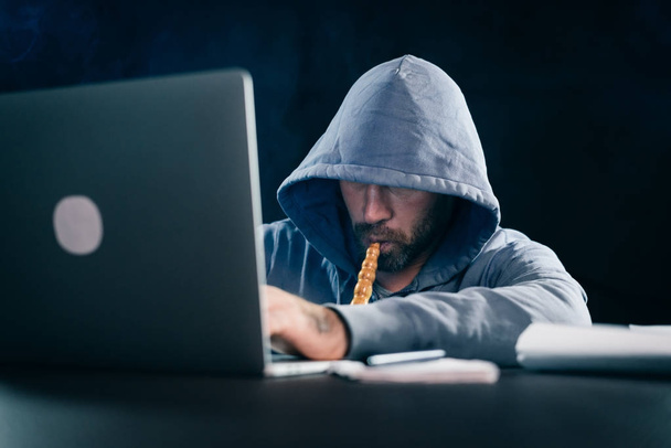 a young hacker guy sits behind a laptop smoking a hookah - Фото, зображення