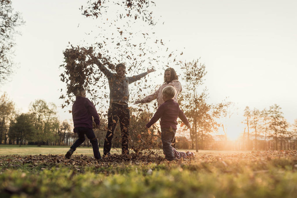 Νεαρή οικογένεια χαίρεσαι για ένα φθινοπωρινό ηλιοβασίλεμα στέκεται ρίχνουν lea - Φωτογραφία, εικόνα