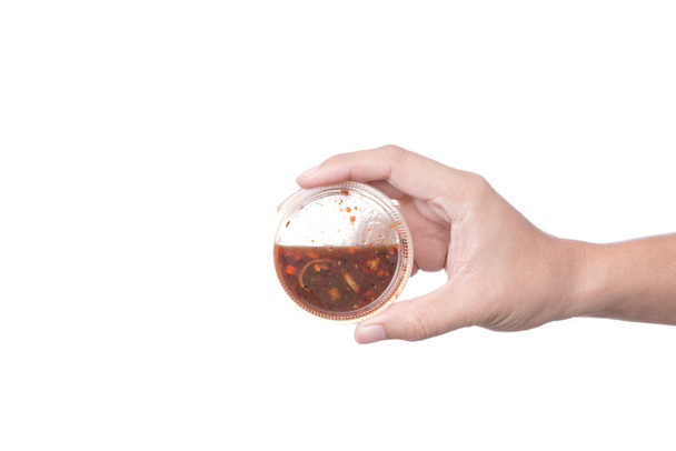 Hand holding plastic cup of sweet fish sauce or shrimp paste chili dip, spicy Thai Nam Prik side dish on white background - Photo, Image
