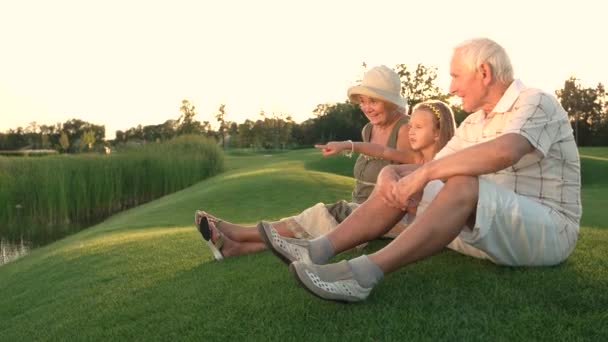 Mädchen und Großeltern sitzen auf Gras. - Filmmaterial, Video