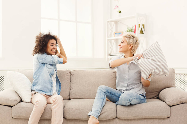 Dos mujeres jóvenes teniendo pelea de almohadas en el sofá
 - Foto, Imagen
