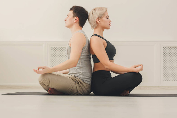 Young couple meditating together, back to back - Foto, afbeelding