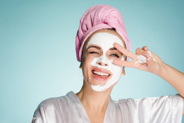 happy girl with a towel on her head apply a cleansing mask on her face - Foto, afbeelding