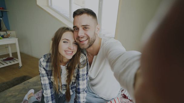 POV shot of cute and loving couple talking online video chat holding smartphone and chatting to friends sitting in bed at home in the morning - Foto, imagen