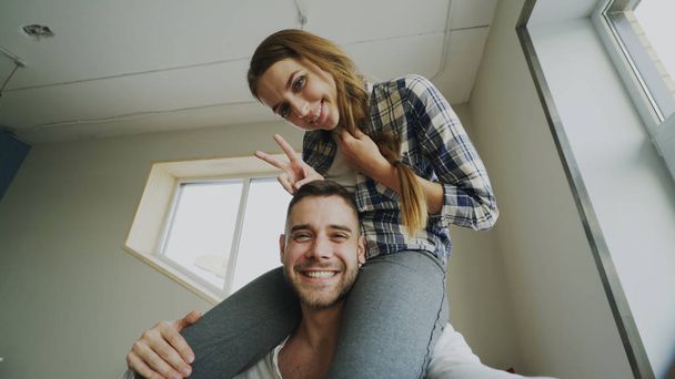 POV of happy smiling and beautiful couple take selfie portrait on smartphone camera while girl sitting on mans neck at home - Photo, image