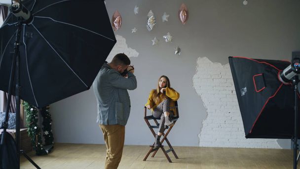 Professional photographer man taking photo of beautiful model girl with digital camera in studio - Fotó, kép