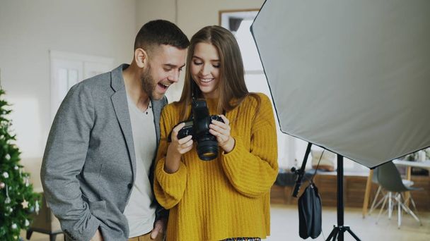 Professional photographer woman showing photos on digital camera to attractive model man in photo studio indoors - Photo, Image
