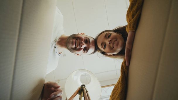 Young happy couple opening cardboard box and looking inside and closing it checking after relocation in new house - 写真・画像