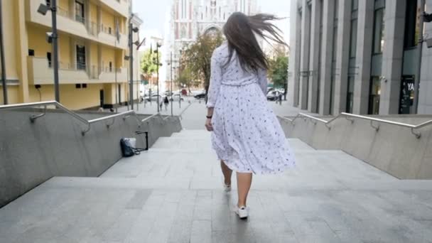 Zwolnionym tempie nagrania wesoła dziewczyna z długimi włosami, chodzenie po schodach kamiennych na ulicy - Materiał filmowy, wideo