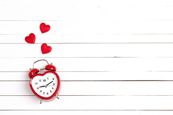 Heart-shaped alarm clock and hearts on white woooden background. - Foto, Imagen