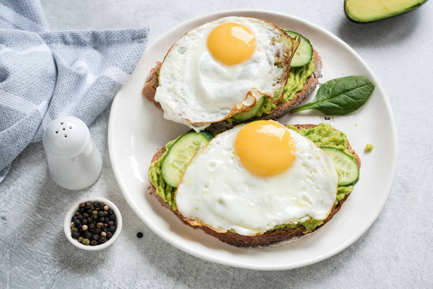Toast with egg, avocado and cucumber on white plate - Fotó, kép