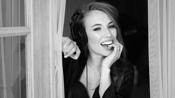 Σέξι γυναίκα ακούγοντας τη μουσική στα ακουστικά. Φορούν σε μαύρη δαντέλα, εσώρουχα και μετάξι ρόμπα. Μαύρο και άσπρο φωτογραφία. - Φωτογραφία, εικόνα