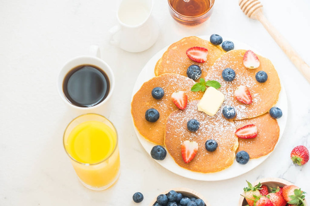 Egészséges reggeli szett palacsinta áfonya és eper gyümölcs és fekete kávé, tej és a narancslé a fehér kő asztal háttere - Fotó, kép