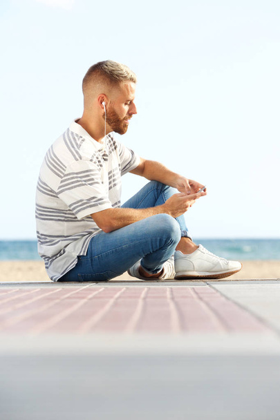 Портрет молодого человека, сидящего на земле и слушающего музыку с наушниками
  - Фото, изображение