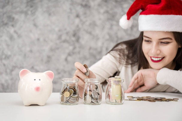 Jeune femme avec chapeau de Noël rouge sautant à la tirelire et la monnaie, concept d'économie pour Noël achats de vacances
. - Photo, image
