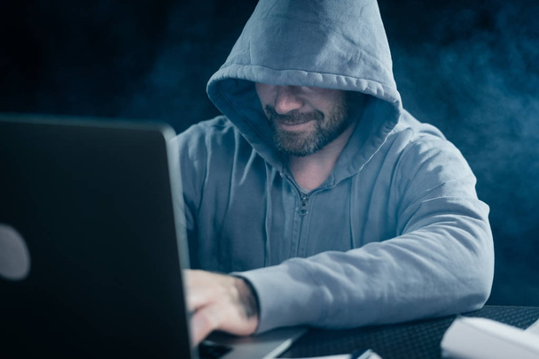 Typ Hacker im Sweatshirt mit Kapuze sitzt hinter einem Laptop - Foto, Bild