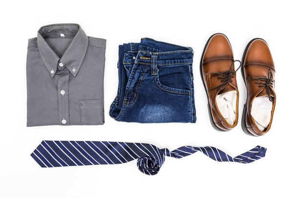 Чоловічий одяг, сорочка, джинси, коричневе взуття та краватка на білому тлі, вид зверху
. - Фото, зображення