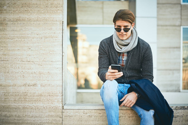 Hombre joven sentado al aire libre y utilizando el teléfono inteligente
. - Foto, Imagen