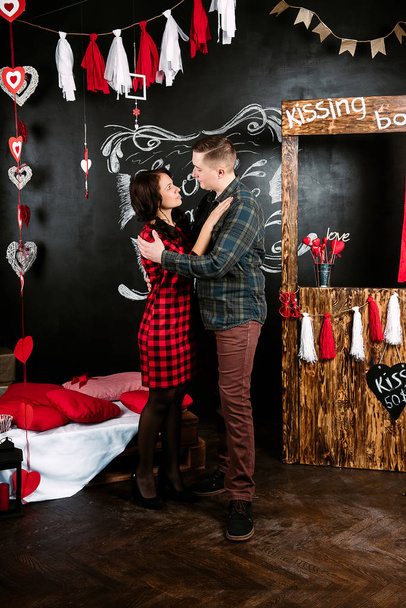 Verliefde omarmen en kussen, jonge vrolijke Europese paar in versierd met harten studio op de dag van de Valentijnskaart, dating. - Foto, afbeelding