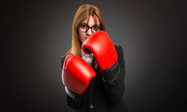 Young business woman with boxing gloves on dark background - 写真・画像