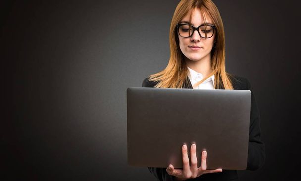 Young business woman with laptop on dark background - Φωτογραφία, εικόνα