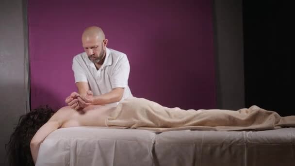 close-up masseur hands doing spine and back massage, relaxed patient enjoys. low key. Man hands massaging female. Spa centre concept - Video, Çekim