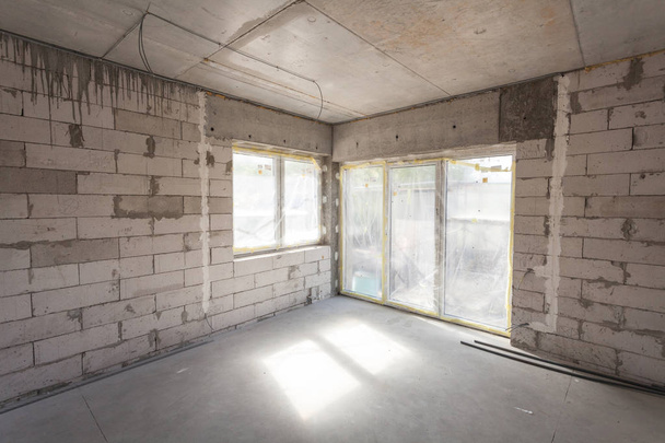 New house under construction. Aerated concrete blocks, cement brickwork walls, plastic window, electric wiring installation. Cement covering in empty room - Photo, Image