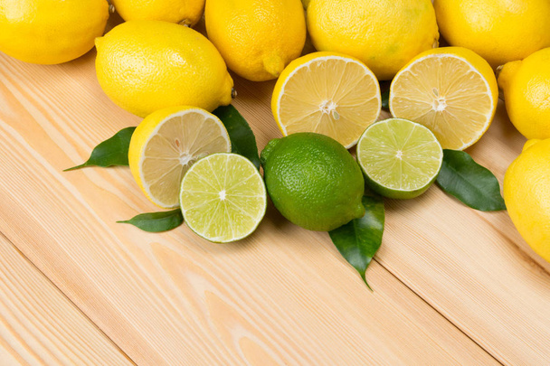 sur une table en bois se trouve des fruits avec du feuillage, du citron vert et des citrons
 - Photo, image