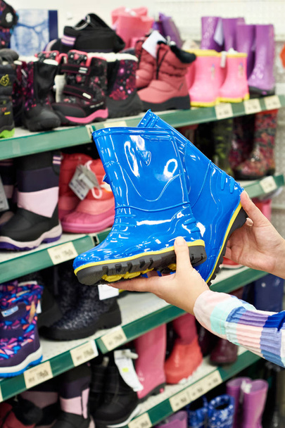 Botas de goma para niños en manos del comprador en la tienda
 - Foto, Imagen