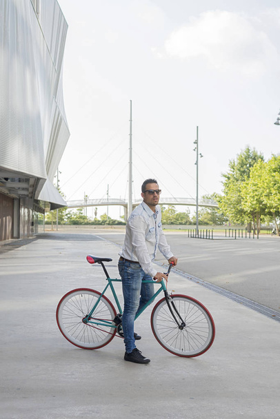 Un giovane uomo elegante con gli occhiali da sole in posa accanto alla sua bicicletta
. - Foto, immagini