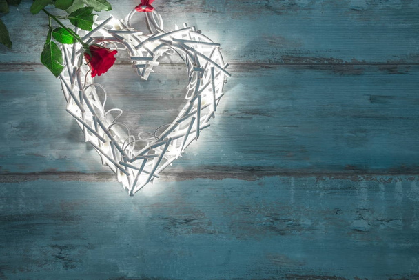 Valentines illuminations in the shape of a heart on a wooden background and red rose. - Foto, afbeelding