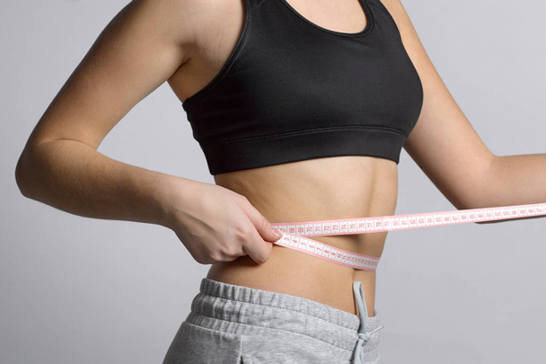 Uma menina em um terno esportivo vai medir sua cintura com um ru flexível
 - Foto, Imagem