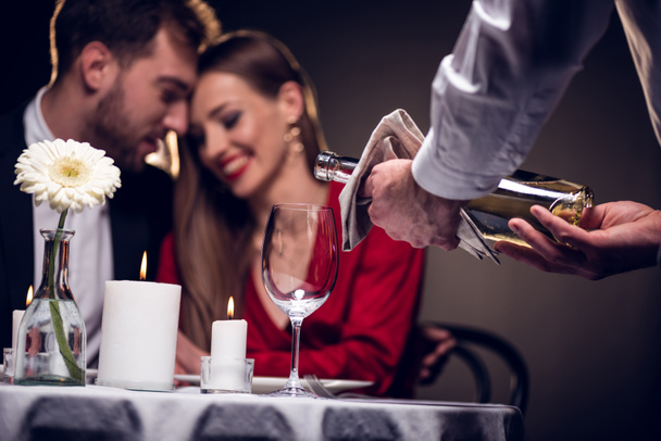 waiter pouring wine while beautiful couple having romantic date in restaurant on valentines day - Photo, Image