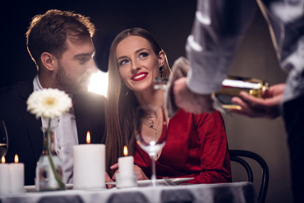 waiter pouring wine while happy couple having romantic date in restaurant on valentines day - Photo, Image