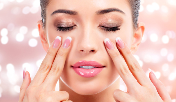 Mulher bonita a massajar o rosto, conceito de tratamento de pele. Fundo abstrato com luzes embaçadas
 - Foto, Imagem