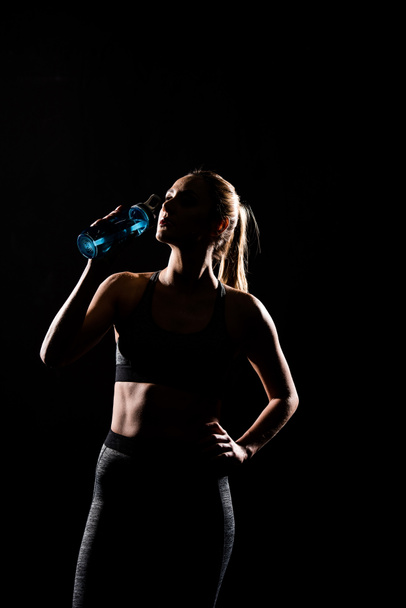 silhouette of sportswoman drinking water from bottle isolated on black - Zdjęcie, obraz