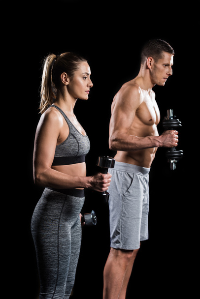 young sportsman and sportswoman exercising with dumbbells isolated on black - Fotoğraf, Görsel