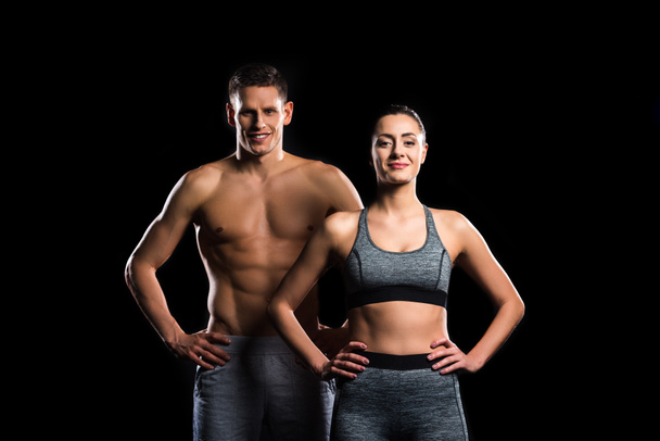 sporty young couple standing together and smiling at camera isolated on black - Photo, Image