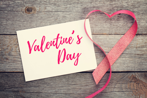 Tarjeta de felicitación de San Valentín en blanco y cinta roja en forma de corazón sobre fondo de madera
 - Foto, Imagen