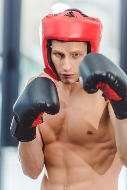 young shirtless muscular boxer looking at camera while boxing in gym   - Фото, зображення