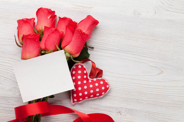 Tarjeta de felicitación del día de San Valentín con rosas rojas y juguete en forma de corazón sobre fondo de madera. Vista superior con espacio
 - Foto, imagen