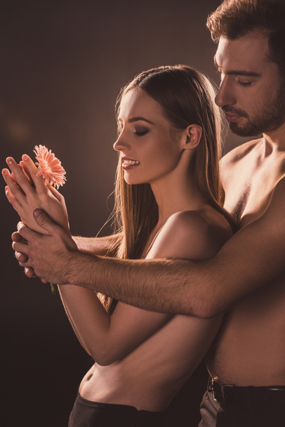 naked lovers hugging and holding flower, on brown - Foto, Imagen