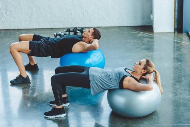 young man and woman exercising on fitness balls in gym - Фото, изображение